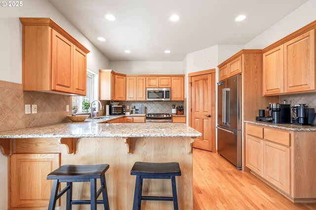 kitchen featuring light stone counters, a breakfast bar area, light wood finished floors, appliances with stainless steel finishes, and a peninsula