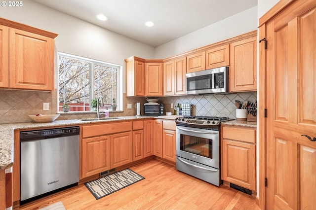 kitchen featuring light wood-style flooring, light stone countertops, stainless steel appliances, a sink, and decorative backsplash