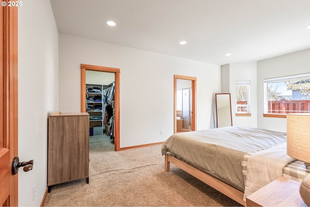 bedroom with a walk in closet, recessed lighting, light carpet, connected bathroom, and baseboards