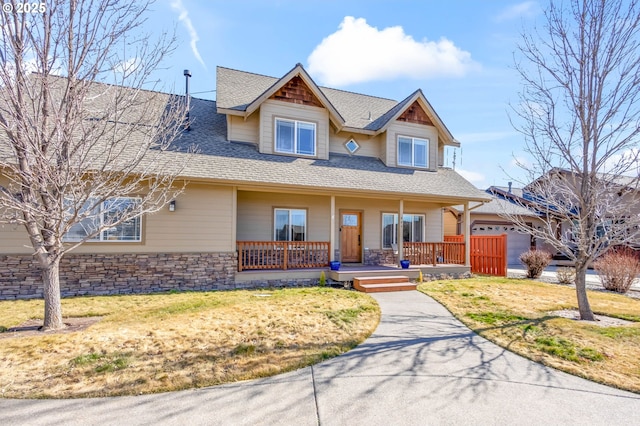 craftsman house with stone siding, a shingled roof, a front lawn, and a porch