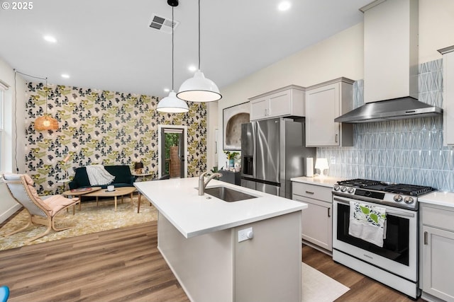 kitchen with wall chimney range hood, appliances with stainless steel finishes, a sink, light countertops, and visible vents