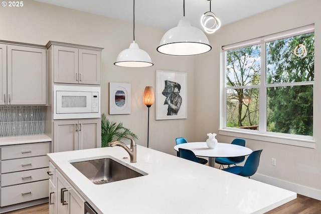 kitchen featuring white microwave, light countertops, a sink, light wood-style flooring, and gray cabinetry