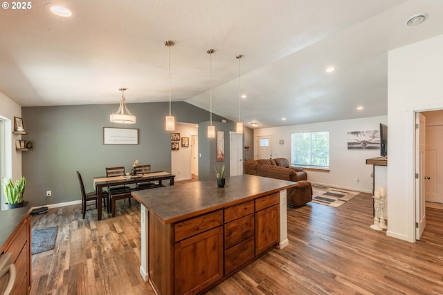 kitchen featuring vaulted ceiling, a kitchen island, wood finished floors, dark countertops, and brown cabinets
