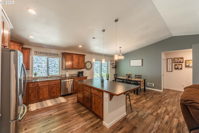 kitchen featuring a breakfast bar, dark wood-style floors, dark countertops, brown cabinets, and appliances with stainless steel finishes