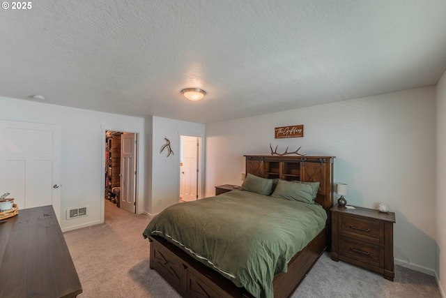 bedroom with a textured ceiling, visible vents, light carpet, a walk in closet, and baseboards