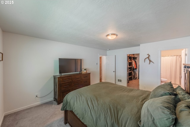 bedroom featuring connected bathroom, a closet, a spacious closet, light carpet, and baseboards