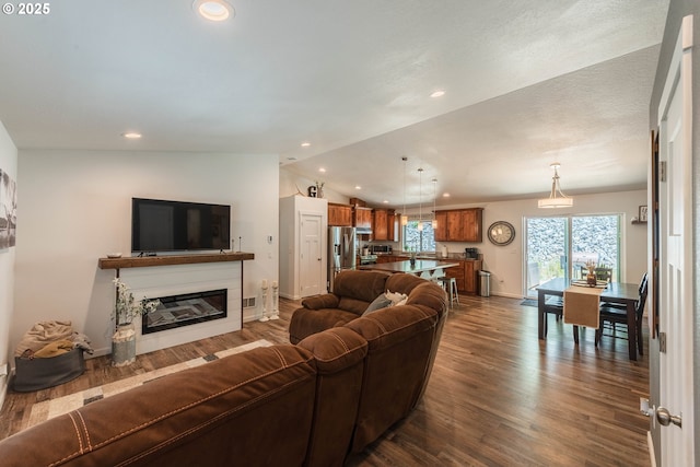 living area with dark wood-type flooring, a glass covered fireplace, vaulted ceiling, recessed lighting, and baseboards