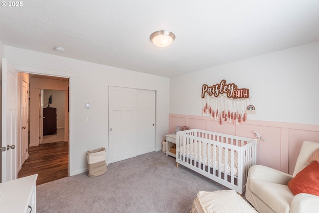 carpeted bedroom with a decorative wall, a closet, and a wainscoted wall