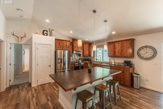 kitchen with brown cabinetry, dark wood-style flooring, a sink, dark countertops, and stainless steel appliances