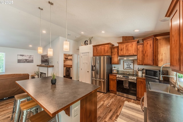 kitchen featuring dark countertops, appliances with stainless steel finishes, under cabinet range hood, brown cabinets, and wood finished floors