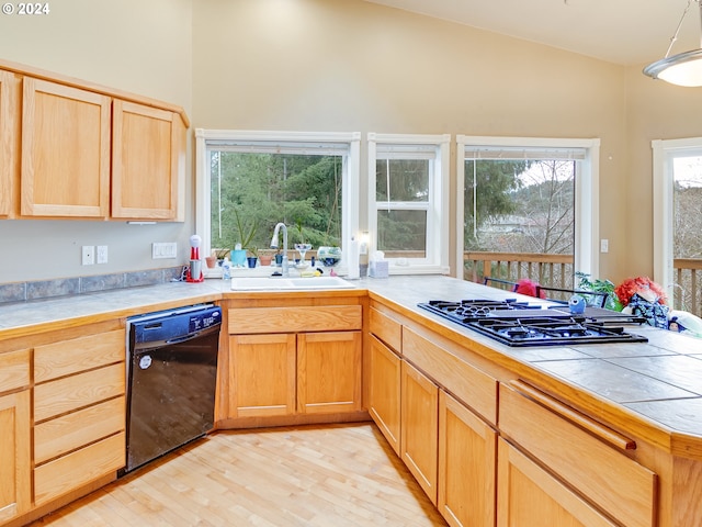 kitchen featuring black dishwasher, stainless steel gas cooktop, tile counters, light wood-style floors, and a sink