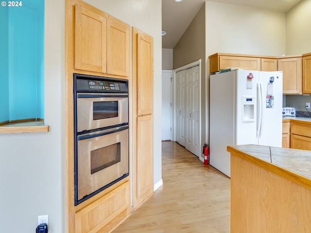 kitchen featuring double oven, light brown cabinets, tile counters, white fridge with ice dispenser, and light wood finished floors