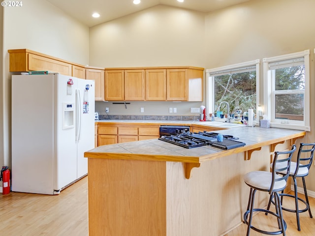 kitchen with tile counters, a breakfast bar, white fridge with ice dispenser, high vaulted ceiling, and a sink