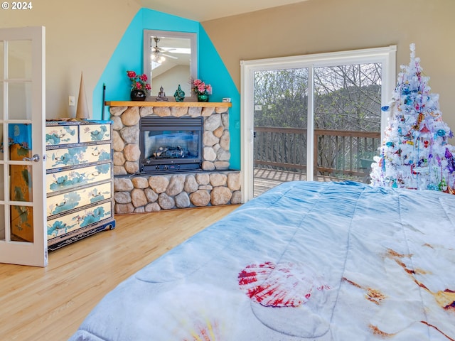 bedroom featuring lofted ceiling, a stone fireplace, wood finished floors, and access to exterior