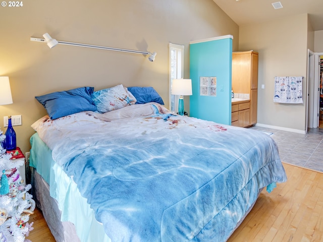 bedroom featuring light wood-type flooring, lofted ceiling, visible vents, and baseboards