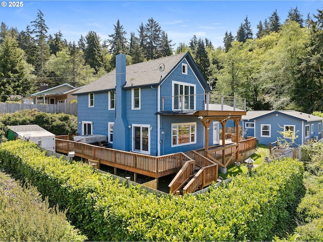 rear view of property with a chimney, roof with shingles, a wooden deck, fence, and a balcony