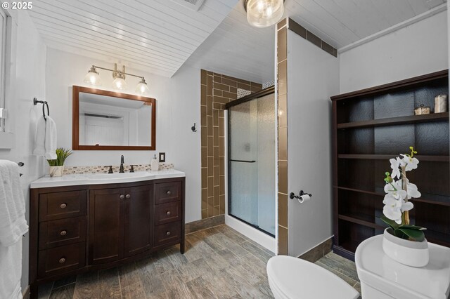 bathroom with vanity, wood finished floors, toilet, baseboards, and a shower stall