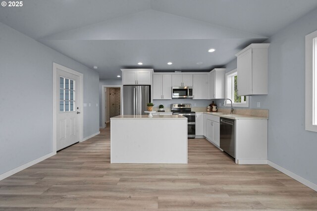kitchen featuring lofted ceiling, a center island, light countertops, white cabinets, and stainless steel appliances