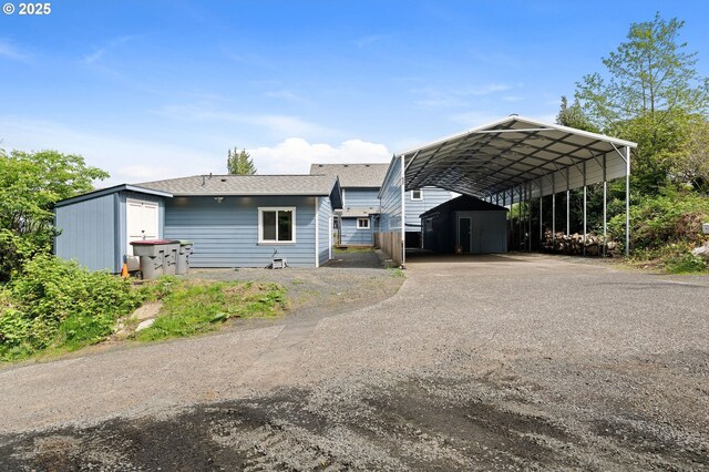 view of front of house with a storage unit, dirt driveway, an outdoor structure, and a detached carport