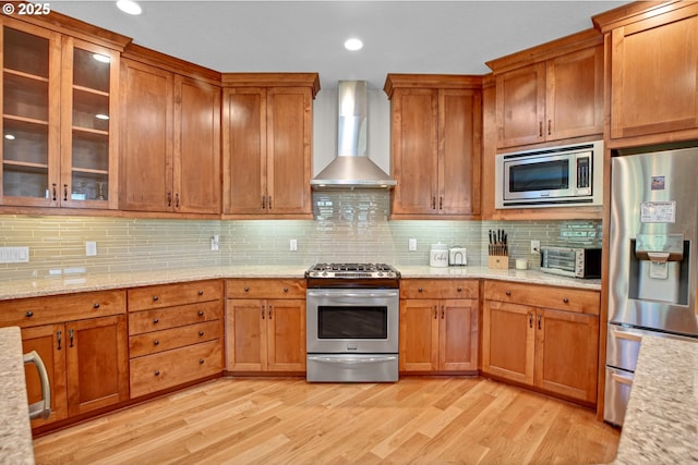 kitchen featuring brown cabinetry, tasteful backsplash, wall chimney range hood, and stainless steel appliances