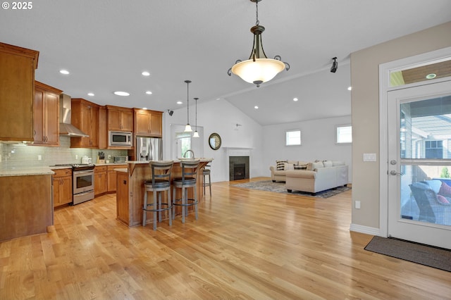 kitchen with appliances with stainless steel finishes, light countertops, a breakfast bar area, wall chimney exhaust hood, and open floor plan