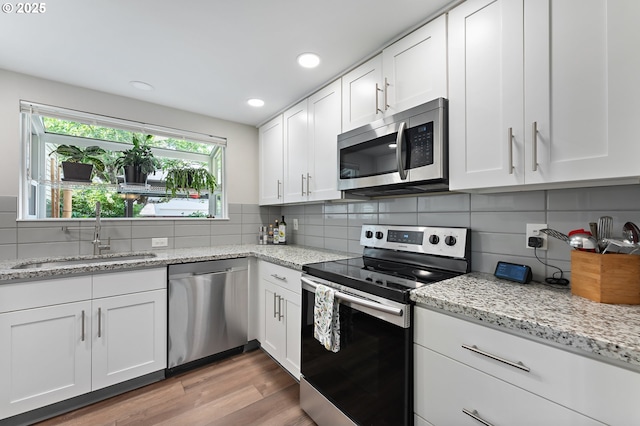 16760 SW Monaco Ln, Portland, OR 97224 - kitchen with stainless steel appliances, white cabinetry, tasteful backsplash, light wood finished floors, and light stone counters