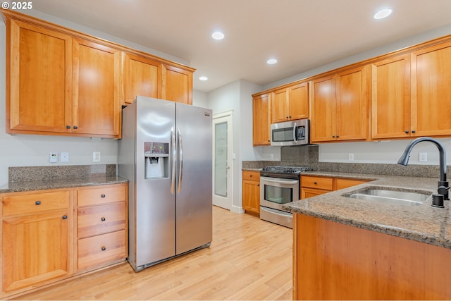 kitchen with appliances with stainless steel finishes, light stone countertops, sink, and light wood-type flooring