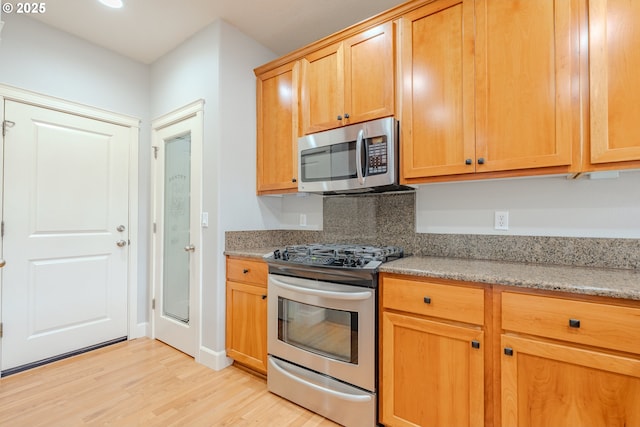 kitchen featuring light stone countertops, appliances with stainless steel finishes, and light hardwood / wood-style flooring