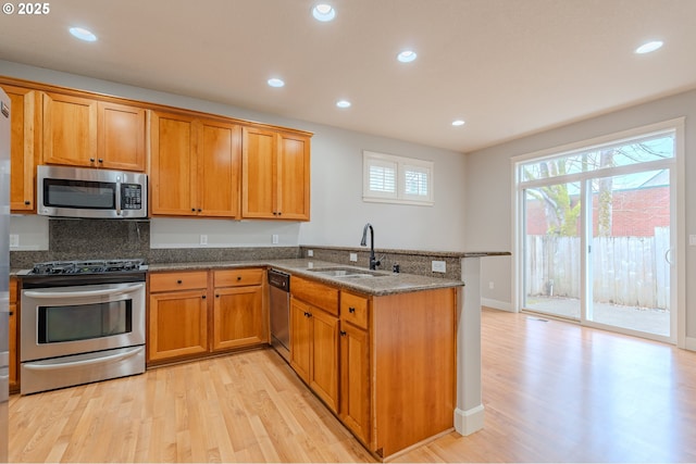 kitchen with sink, dark stone counters, kitchen peninsula, stainless steel appliances, and light hardwood / wood-style floors