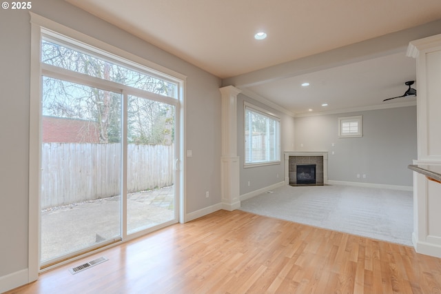 unfurnished living room with ornate columns, crown molding, light hardwood / wood-style flooring, a tile fireplace, and ceiling fan