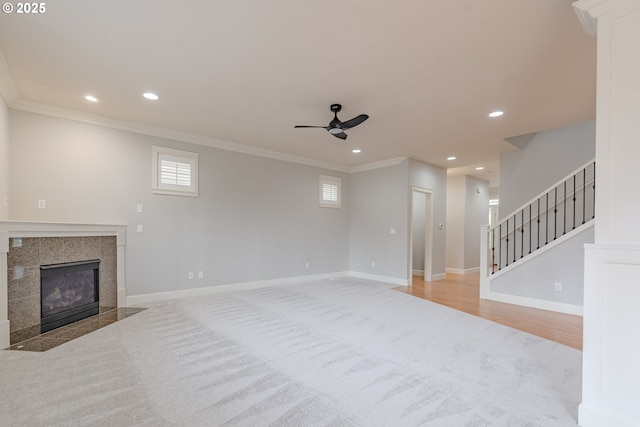 living room featuring a tiled fireplace, ornamental molding, light carpet, and ceiling fan