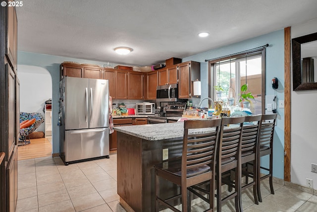 kitchen featuring stainless steel appliances, light countertops, a peninsula, a kitchen bar, and light tile patterned floors