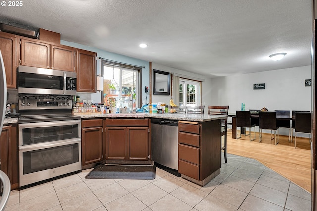 kitchen with stainless steel appliances, a peninsula, a textured ceiling, recessed lighting, and light tile patterned floors