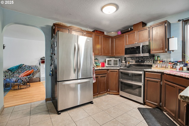 kitchen featuring appliances with stainless steel finishes, arched walkways, light tile patterned floors, and a textured ceiling