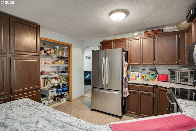 kitchen with freestanding refrigerator, light tile patterned flooring, arched walkways, a textured ceiling, and range with electric cooktop