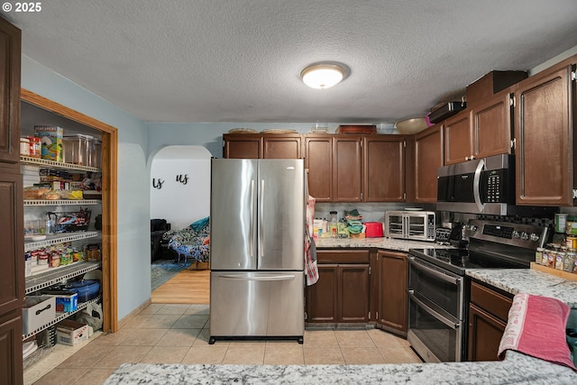 kitchen with stainless steel appliances, light tile patterned floors, arched walkways, and a textured ceiling