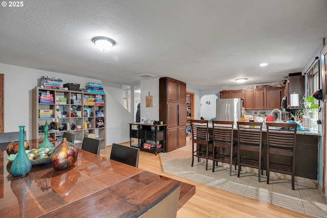 dining space with light wood finished floors, a textured ceiling, and recessed lighting