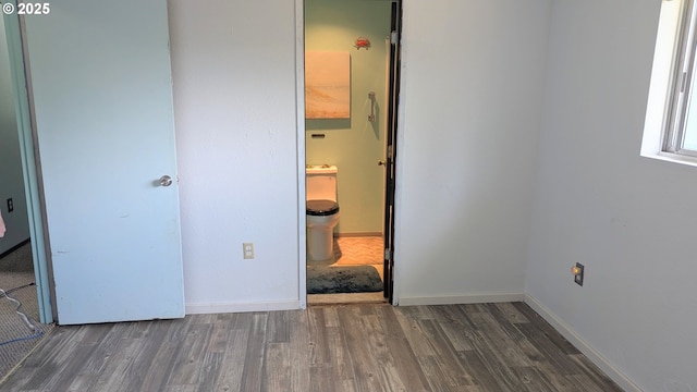 unfurnished bedroom featuring connected bathroom, baseboards, and wood finished floors