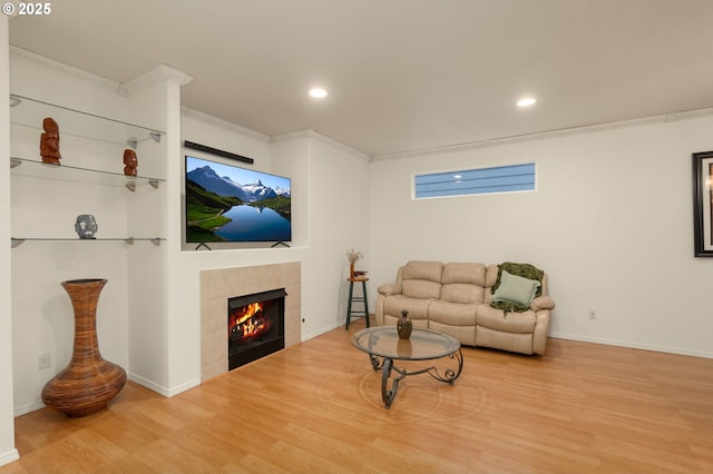 living area with baseboards, a tiled fireplace, ornamental molding, recessed lighting, and wood finished floors