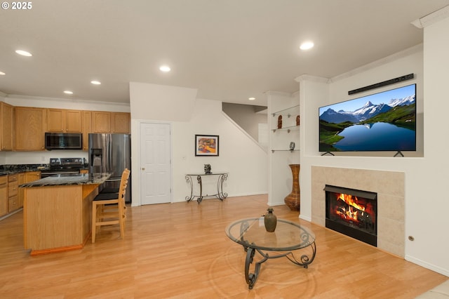 living room with recessed lighting, crown molding, a tiled fireplace, and light wood finished floors