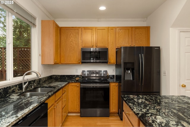 kitchen with black appliances, light wood-style flooring, dark stone countertops, and a sink