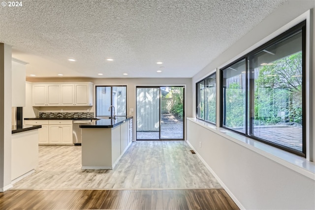 kitchen featuring a textured ceiling, stainless steel dishwasher, white cabinets, and light hardwood / wood-style floors