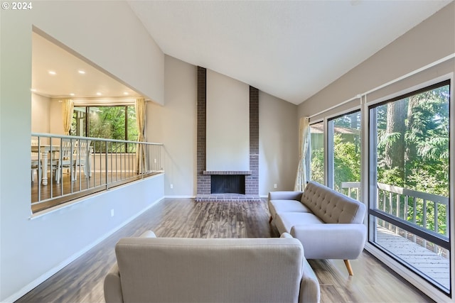 living room with hardwood / wood-style floors, vaulted ceiling, and a brick fireplace