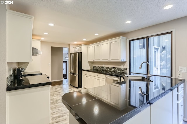 kitchen with appliances with stainless steel finishes, white cabinets, light hardwood / wood-style floors, kitchen peninsula, and a textured ceiling