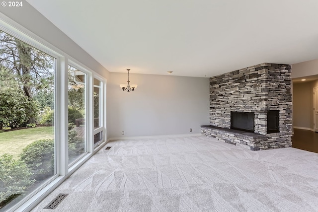 unfurnished living room with a wealth of natural light, a stone fireplace, light colored carpet, and a notable chandelier