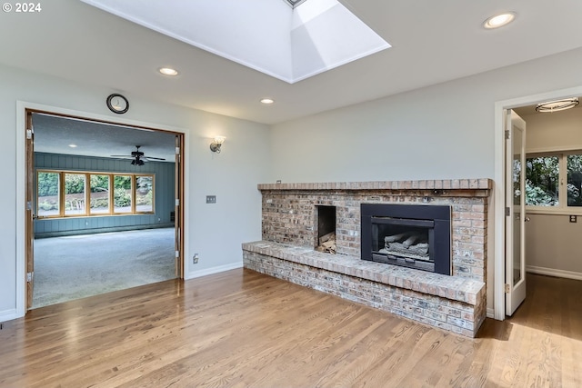 living room featuring a fireplace, wood-type flooring, a skylight, and ceiling fan