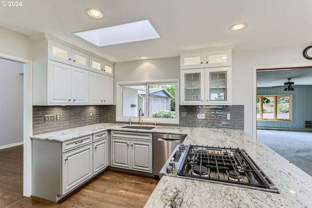 kitchen with sink, a skylight, stainless steel dishwasher, ceiling fan, and white cabinets