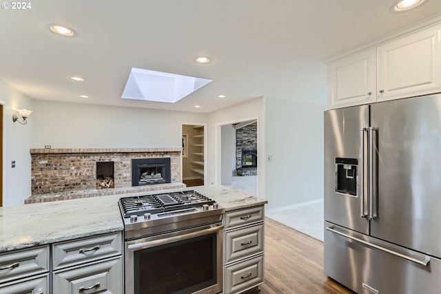 kitchen with white cabinetry, a skylight, appliances with stainless steel finishes, built in features, and light stone countertops