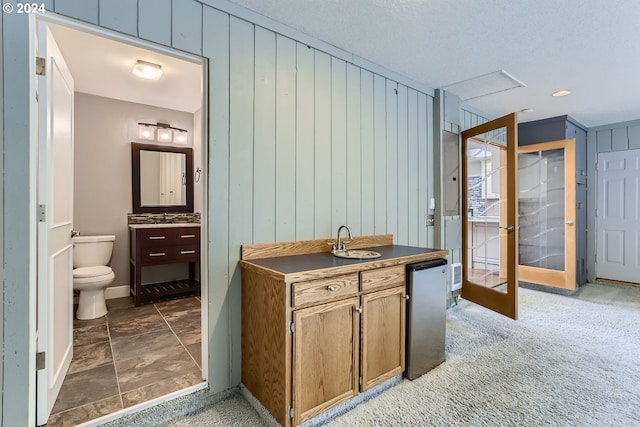 interior space featuring french doors, toilet, wood walls, a textured ceiling, and vanity