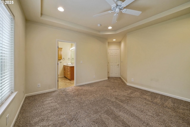 unfurnished bedroom featuring a raised ceiling, light carpet, and ensuite bath